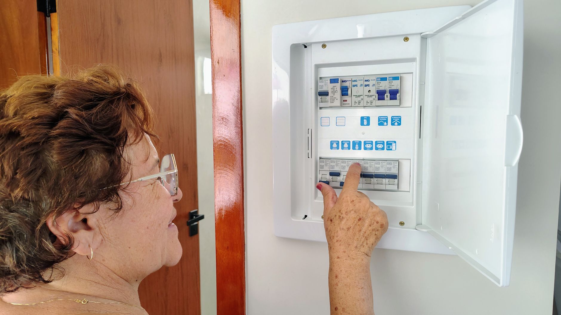 A senior woman is adjusting an electrical fuse panel indoors, demonstrating home safety.