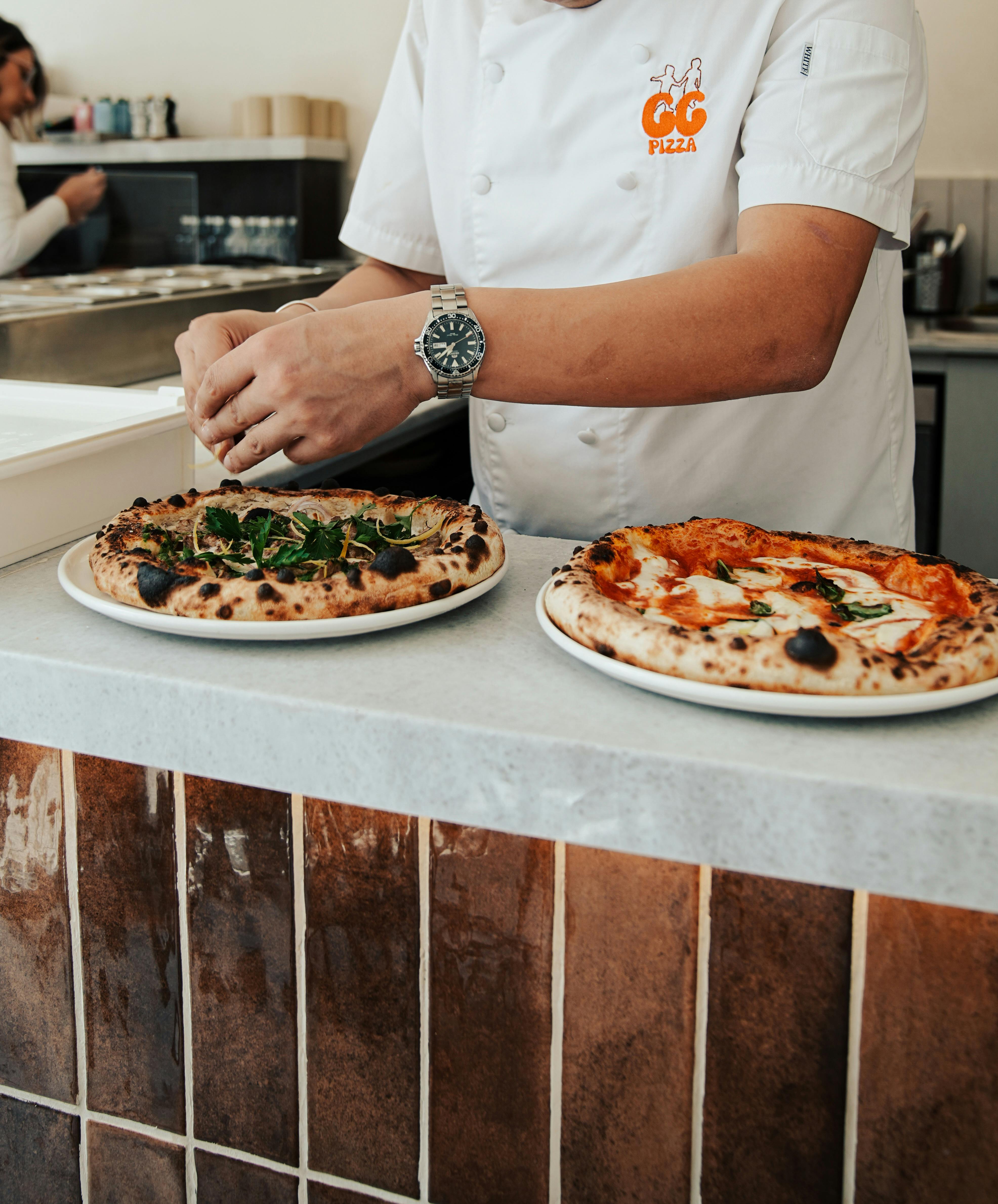 Chef garnishing delicious artisan pizzas in a modern kitchen.