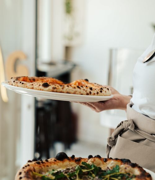 Free Server presenting warm pizza in a cozy restaurant setting. Stock Photo