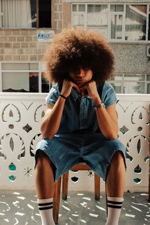 Free Young adult with afro hairstyle sitting outdoors on a sunny day. Stock Photo