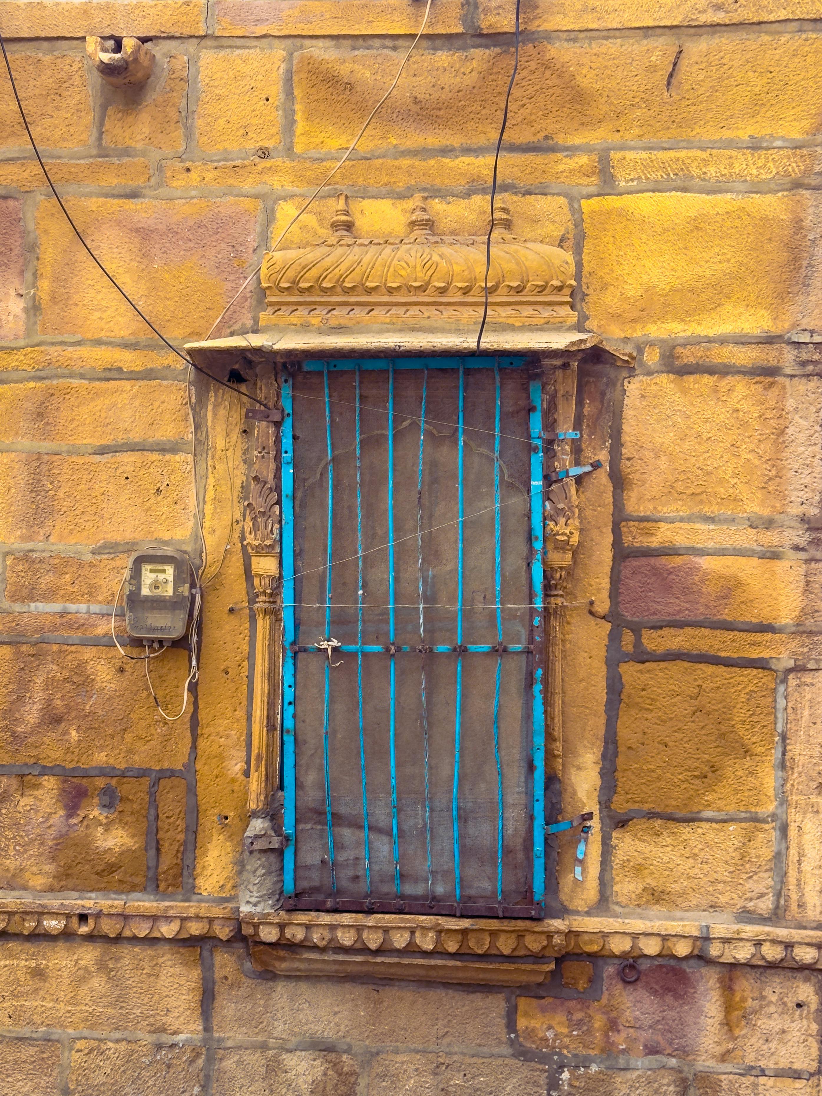 Captivating vintage window with blue bars on a yellow stone wall in Jodhpur, Rajasthan.