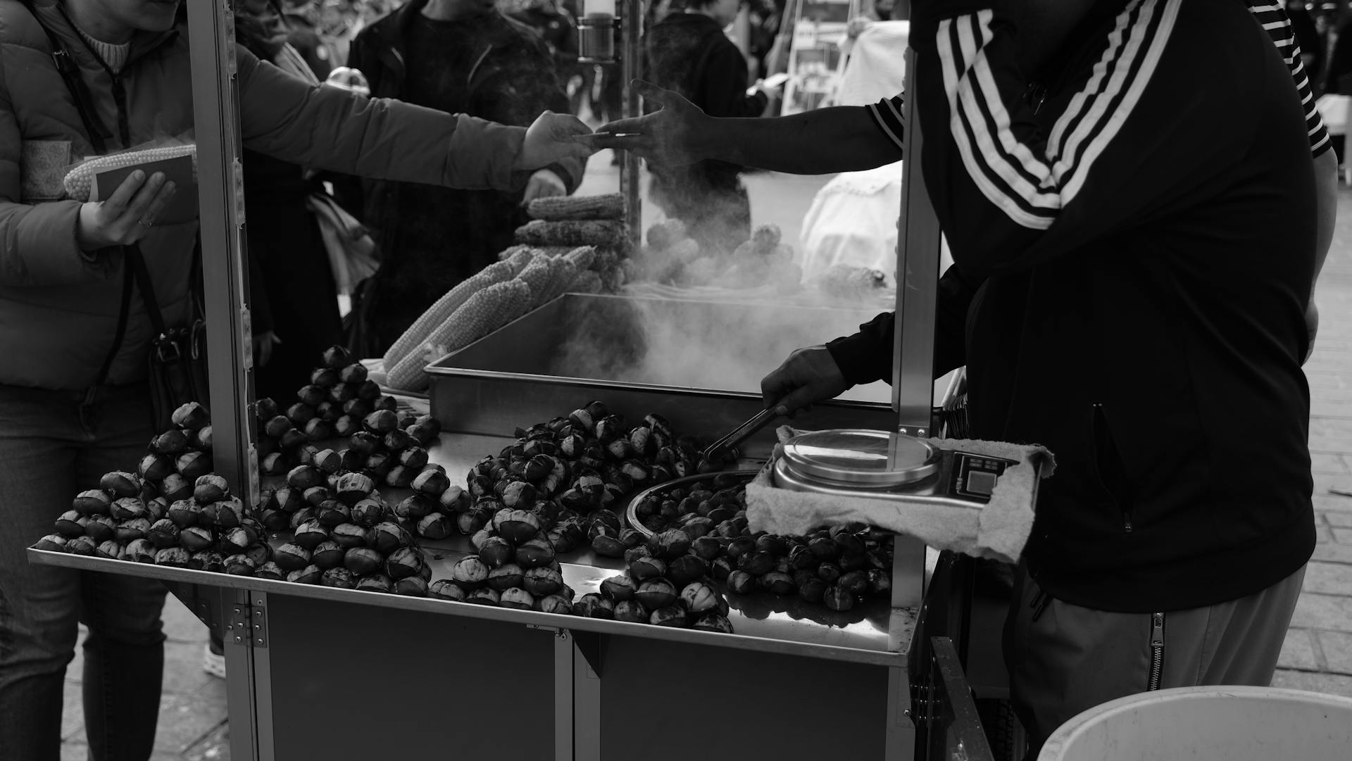 A bustling street market scene with a vendor selling roasted chestnuts to customers.