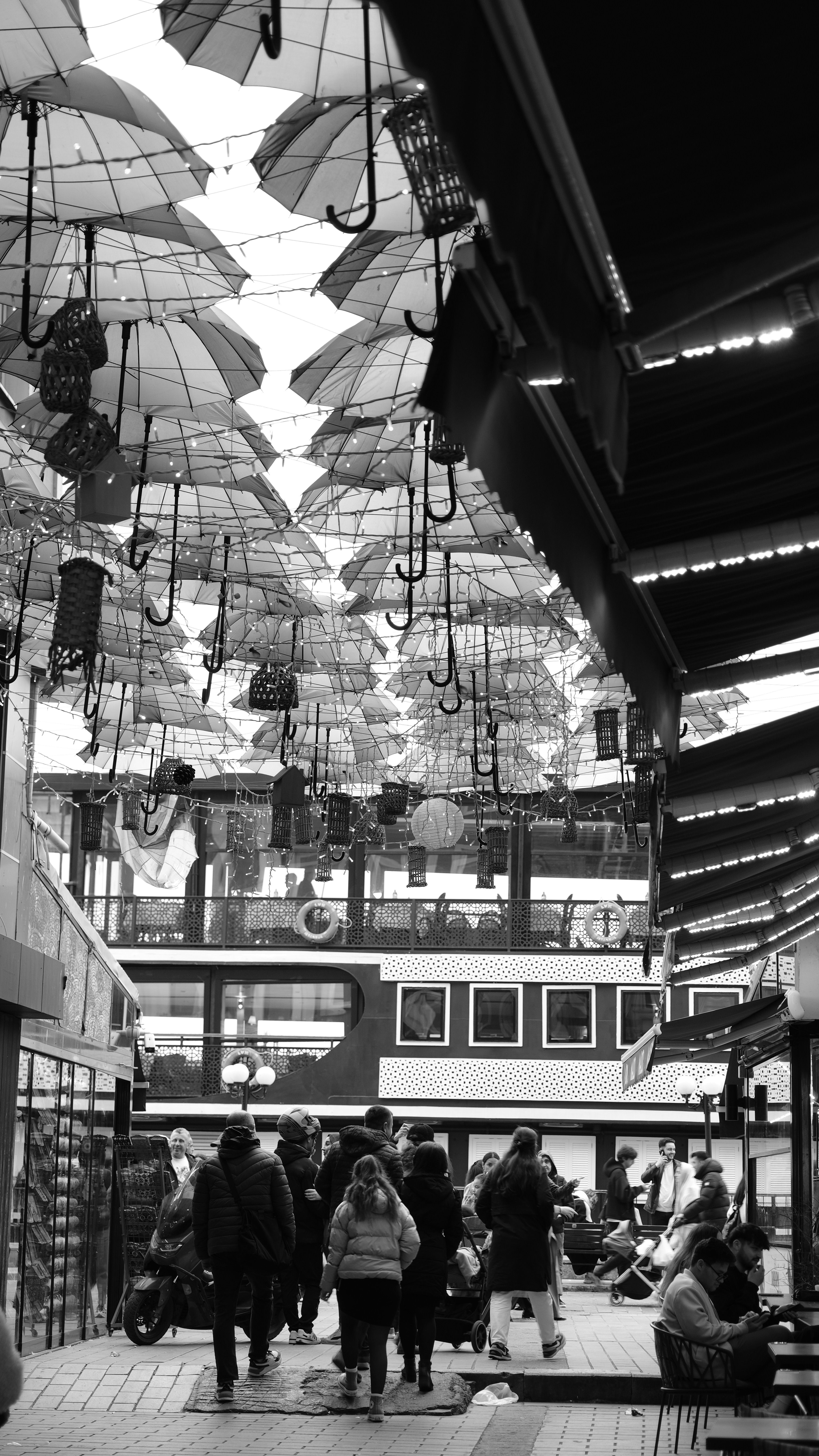Monochrome view of a bustling street with hanging umbrellas decorating overhead.