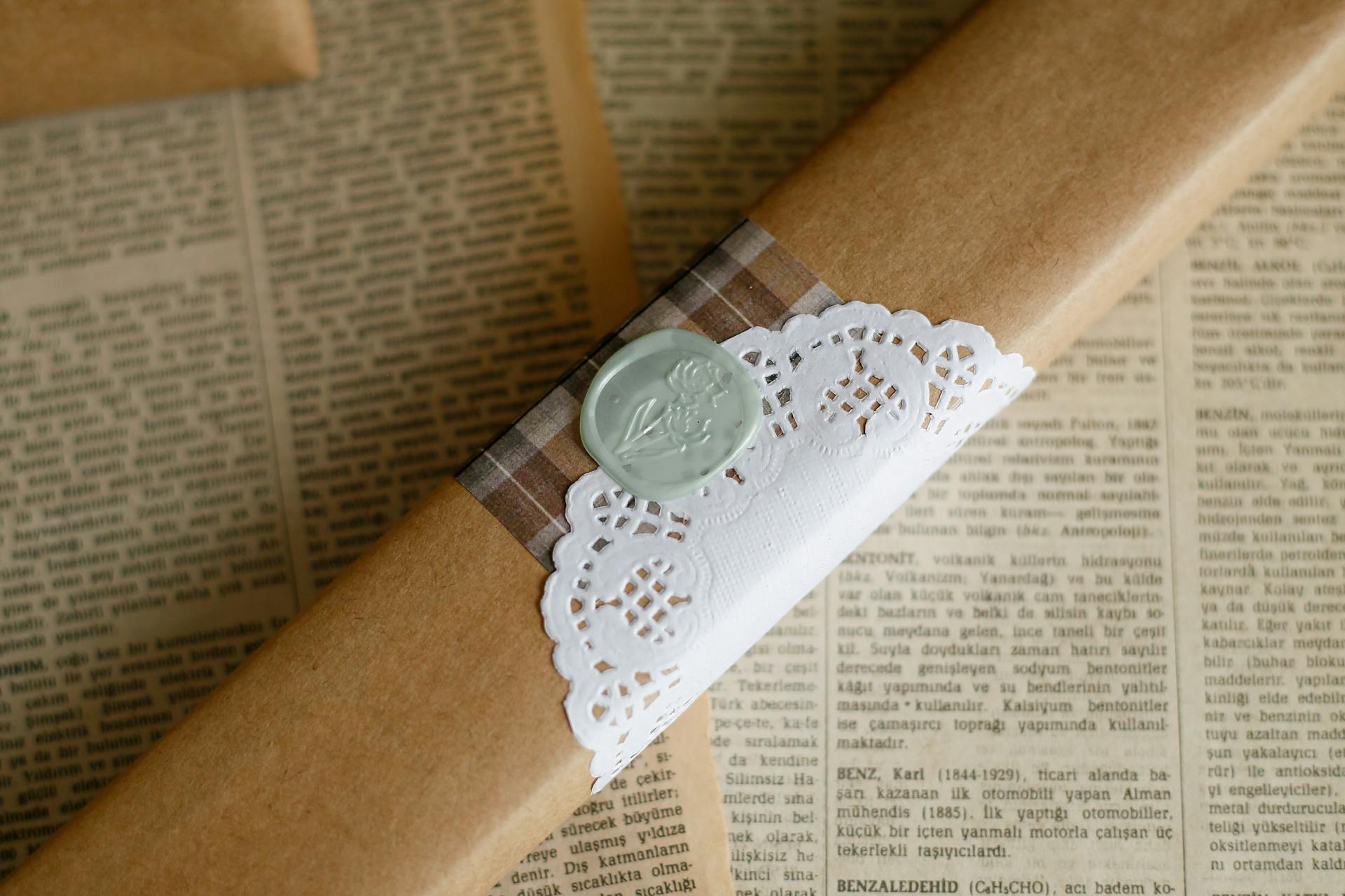 Close-up of an elegantly wrapped gift with a wax seal and lace detail on vintage newspaper background.