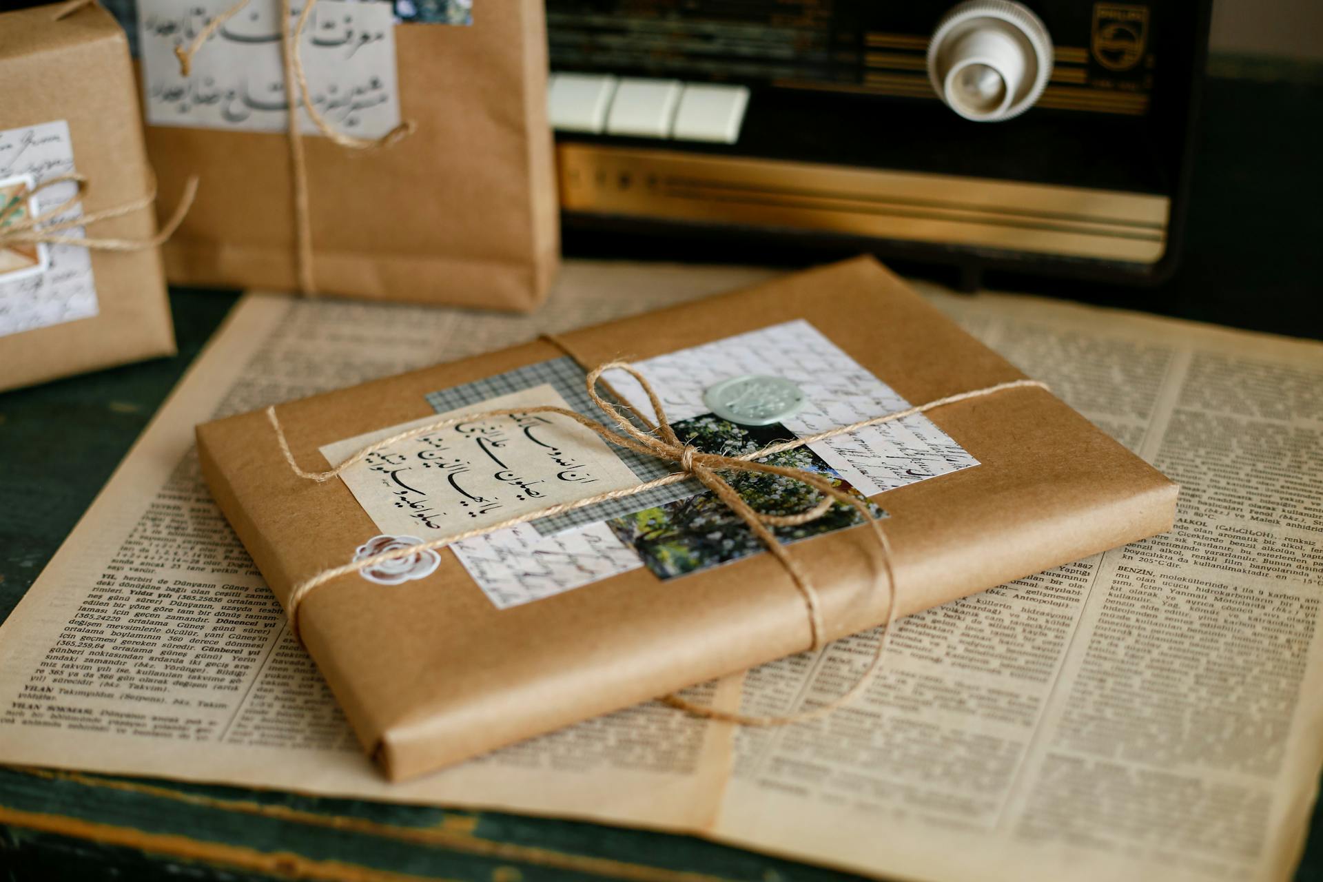 A vintage-styled brown paper wrapped parcel tied with string, featuring Arabic script and old radio, placed on aged book pages.