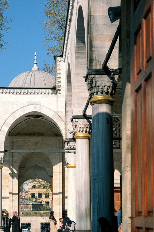 Free Sunlit archways and columns at a historic mosque with people in the courtyard. Stock Photo