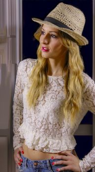 Fashionable woman wearing a lace top and straw hat posing indoors with a stylish look.