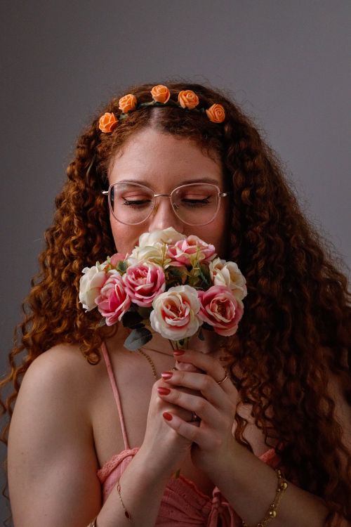 Free A young woman with glasses enjoying the fragrance of a rose bouquet indoors. Stock Photo
