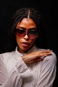 Elegant woman wearing sunglasses and a white blouse against a dark backdrop.
