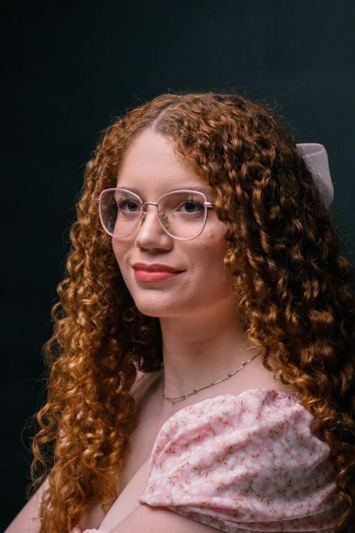 Free Close-up portrait of a woman with curly red hair and glasses wearing a pink dress. Stock Photo