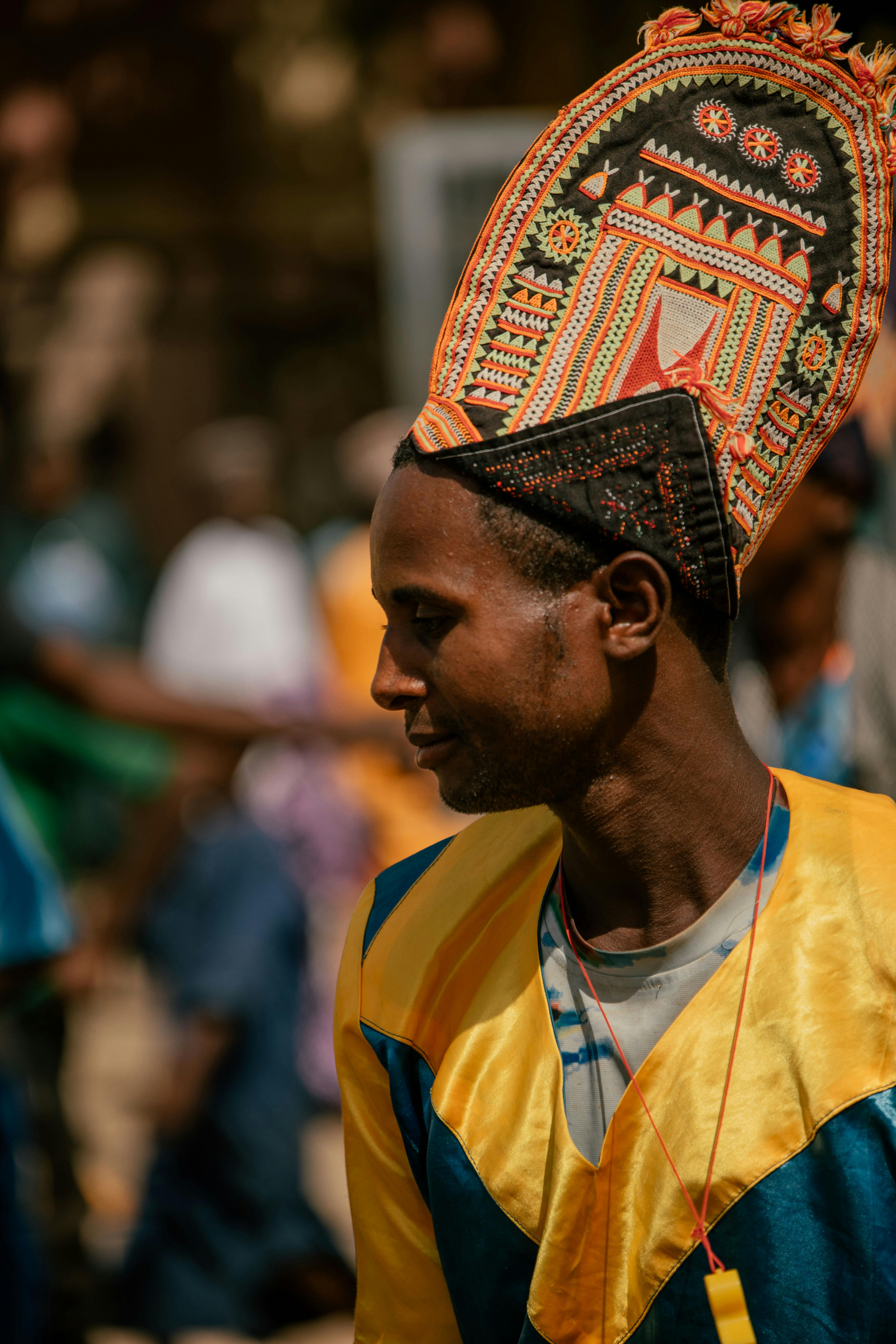 A man in colorful attire and ornate headdress at an outdoor cultural festival.