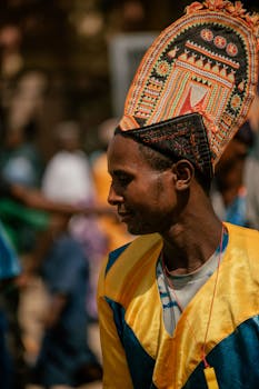A man in colorful attire and ornate headdress at an outdoor cultural festival.