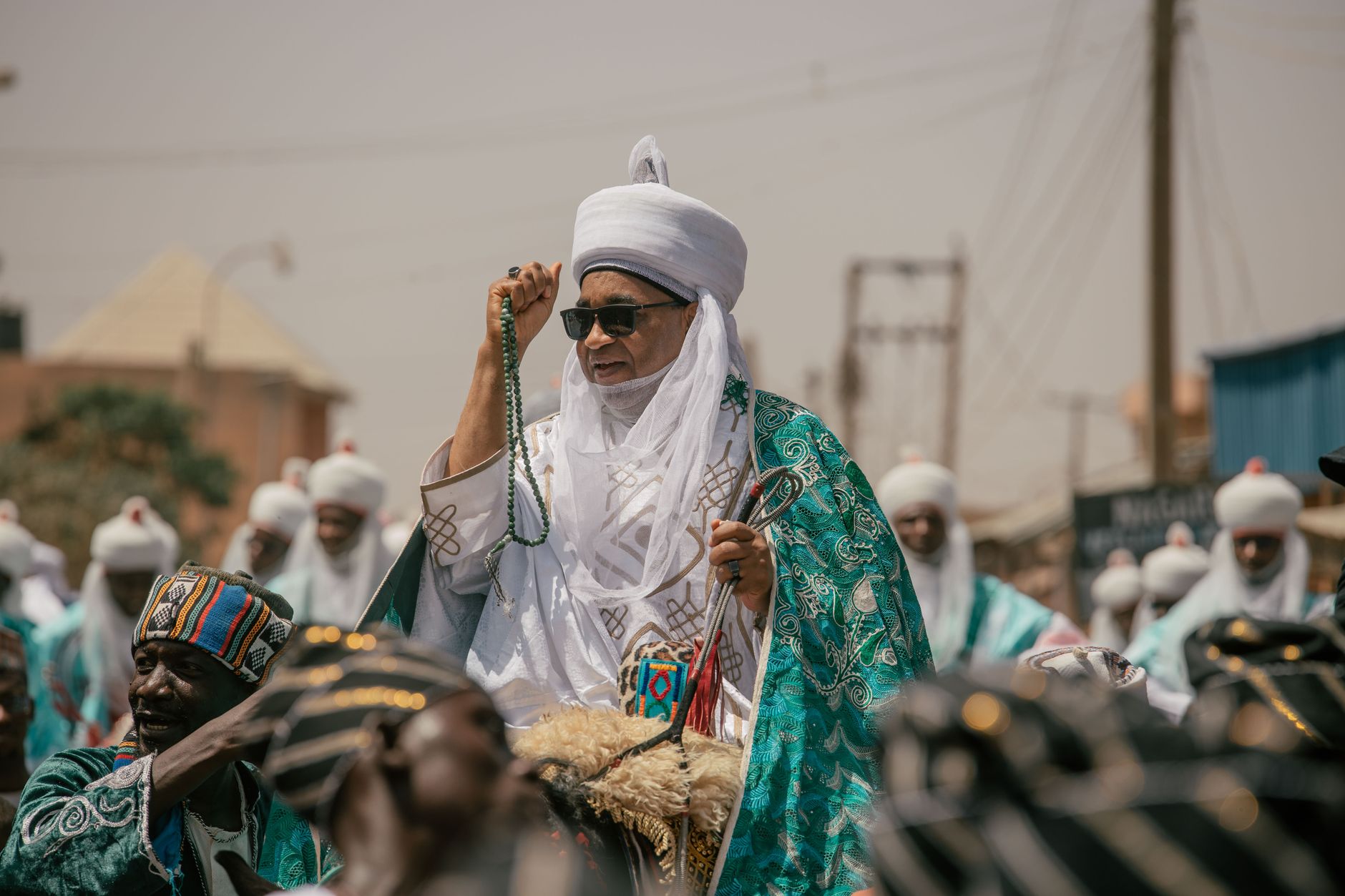 A traditional African chief dressed in vibrant attire participates in a cultural parade outdoors.