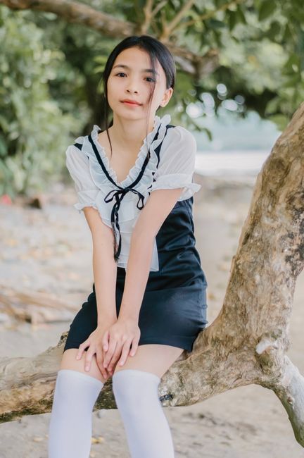Charming young Asian female sitting on a tree branch outdoors, exuding casual and fashionable style.