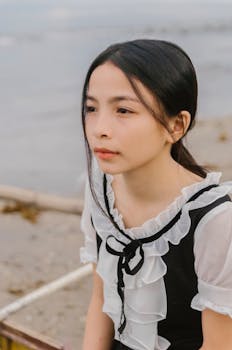 海边，一位亚洲女子身着优雅连衣裙，若有所思地坐着