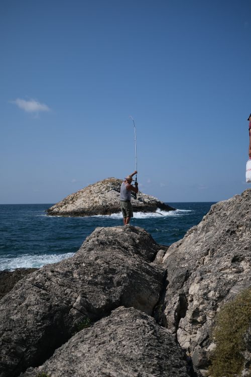 Free A man fishing on a rocky shore with a view of the ocean and distant island. Stock Photo