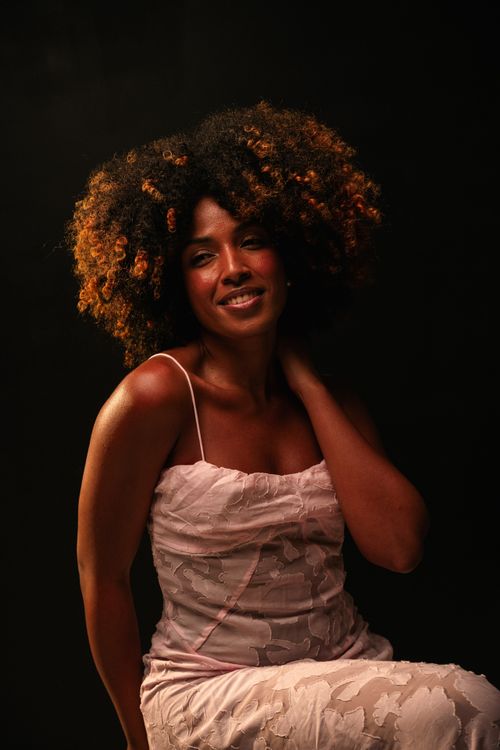 Free Elegant portrait of a woman with afro curls in a light dress against a dark background. Stock Photo