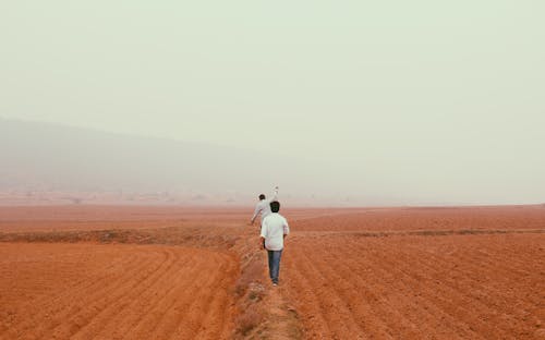 Men in White Shirt Walking on Brown Sand