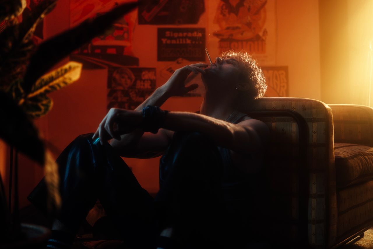 a moody portrait of a man sitting indoors smoking in a warm ambient at