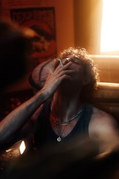A dramatic portrait of a man smoking, illuminated by warm indoor lighting.