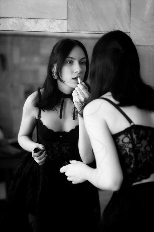 Free Black and white image of a woman applying lipstick in front of a mirror. Stock Photo