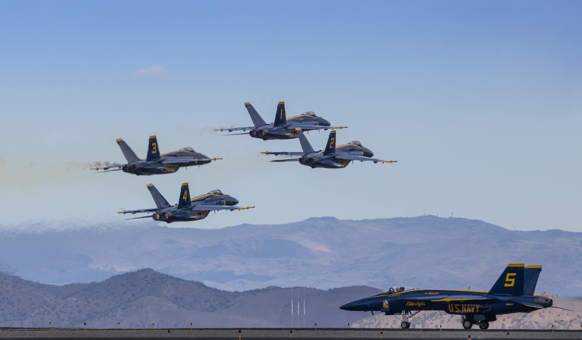 Navy Blue Angels perform precision aerobatics in clear skies over a mountainous landscape.
