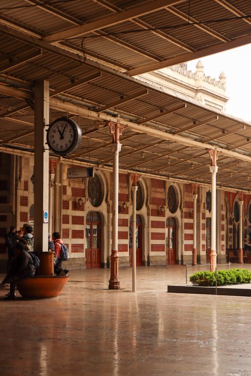 Free Passengers wait under a vintage clock at a historic train station platform. Stock Photo