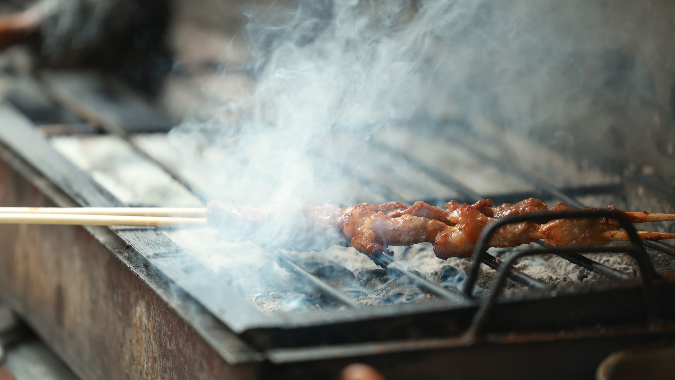 Grilled skewers with smoky aroma on outdoor barbecue. Perfect street food scene.