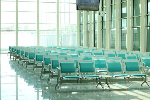 Free Bright airport waiting area featuring rows of empty turquoise chairs and large windows. Stock Photo