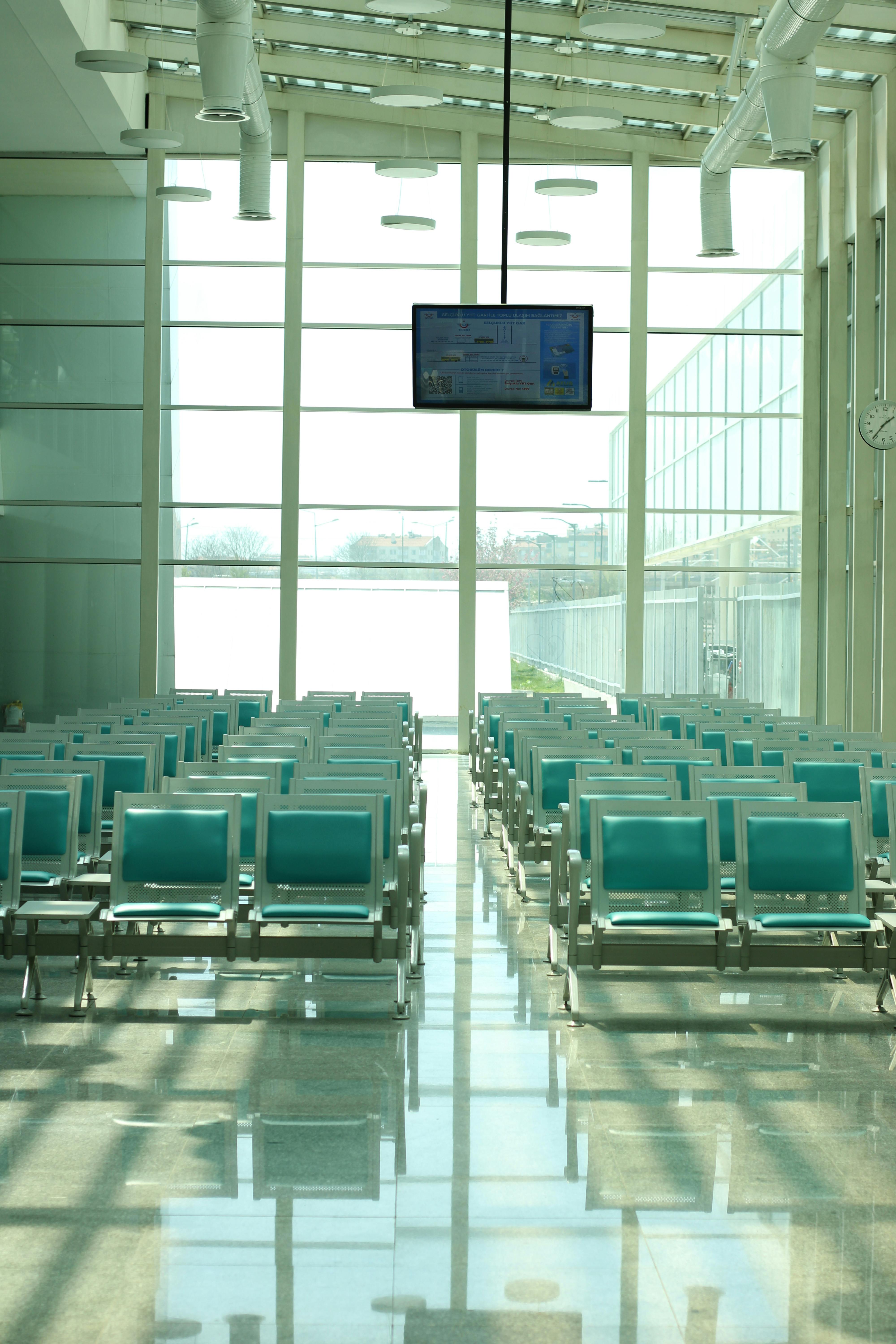 Sunlit airport waiting area with rows of teal seating and modern architecture.