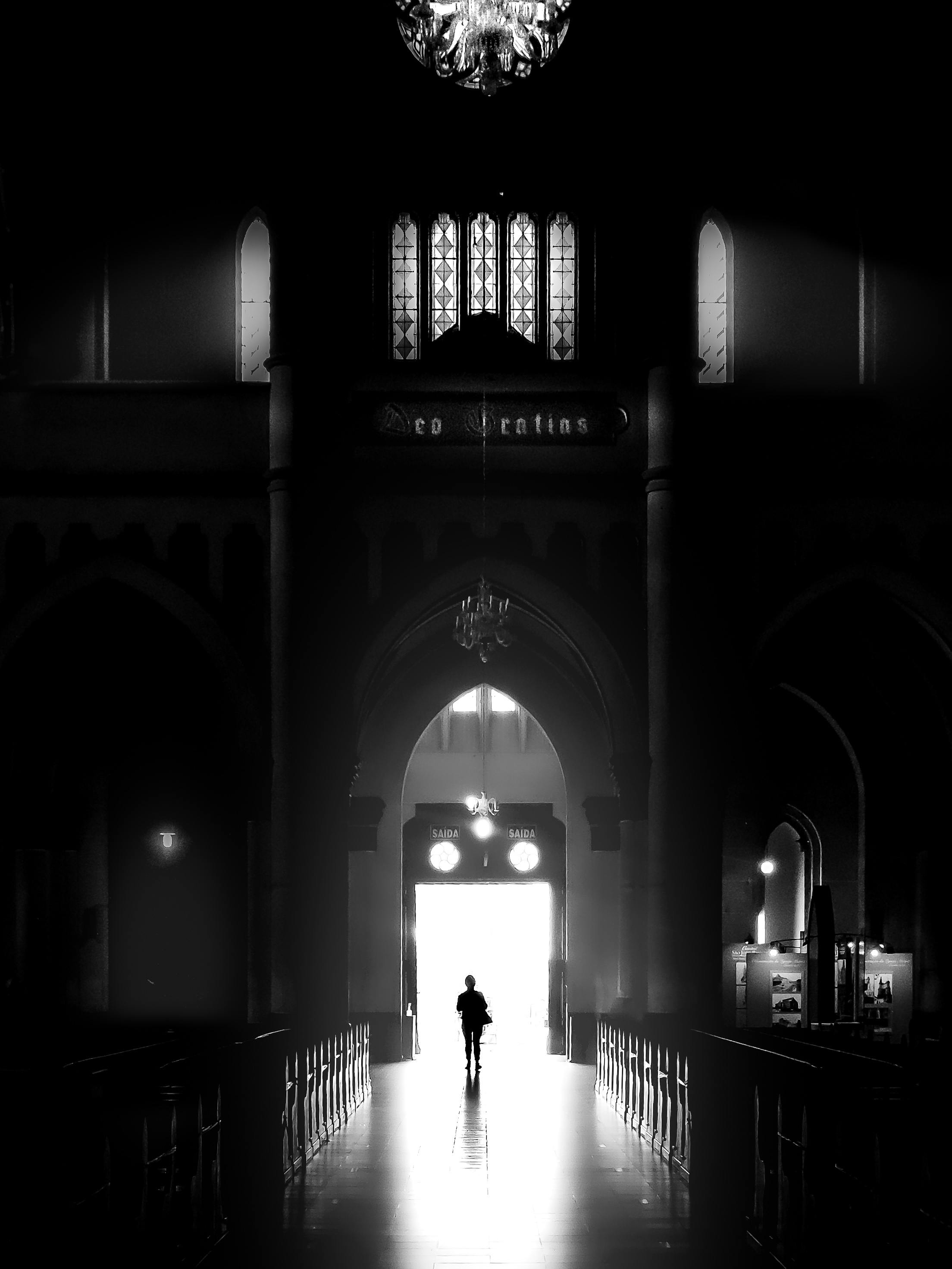 Silhouette of a person walking through a gothic church interior with dramatic lighting.