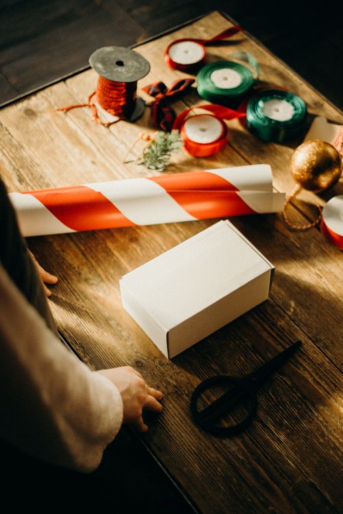 Free A warm depiction of gift wrapping with ribbons, scissors, and decorations on a wooden table. Stock Photo