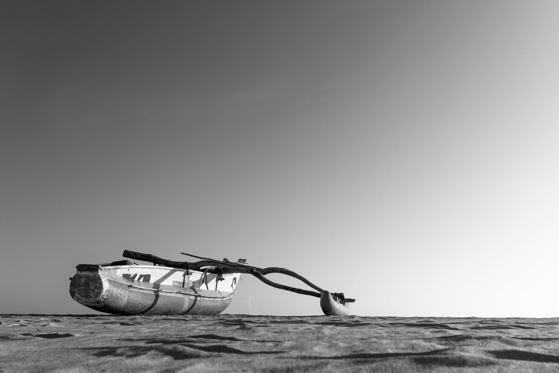 Black and white photo of a traditional fishing boat on a Sri Lankan beach with vast sky.