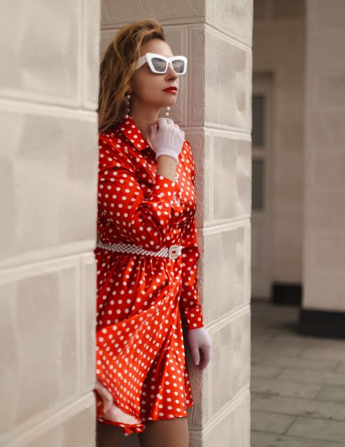 Free Stylish woman in red polka dot dress poses confidently outdoors with sunglasses and gloves. Stock Photo
