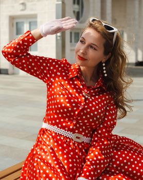 Elegant woman in red polka dot dress with gloves and sunglasses outdoors.