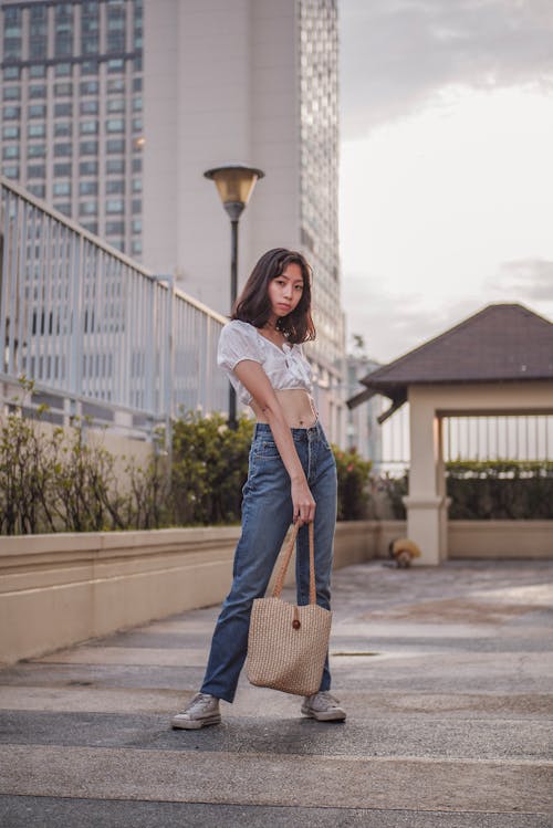 Donna In Camicia Bianca E Jeans Blu Denim Che Tiene Borsa A Tracolla Marrone