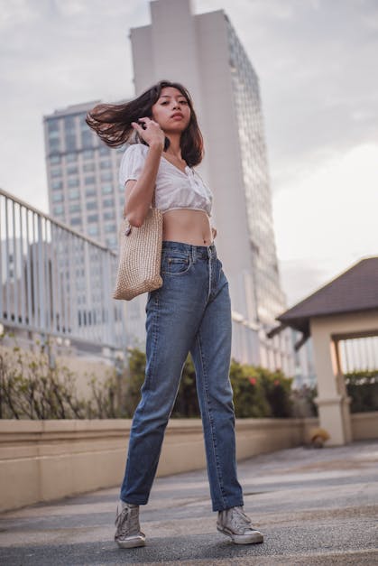 Woman In White Tank Top And Blue Denim Jeans Standing On Gray Concrete