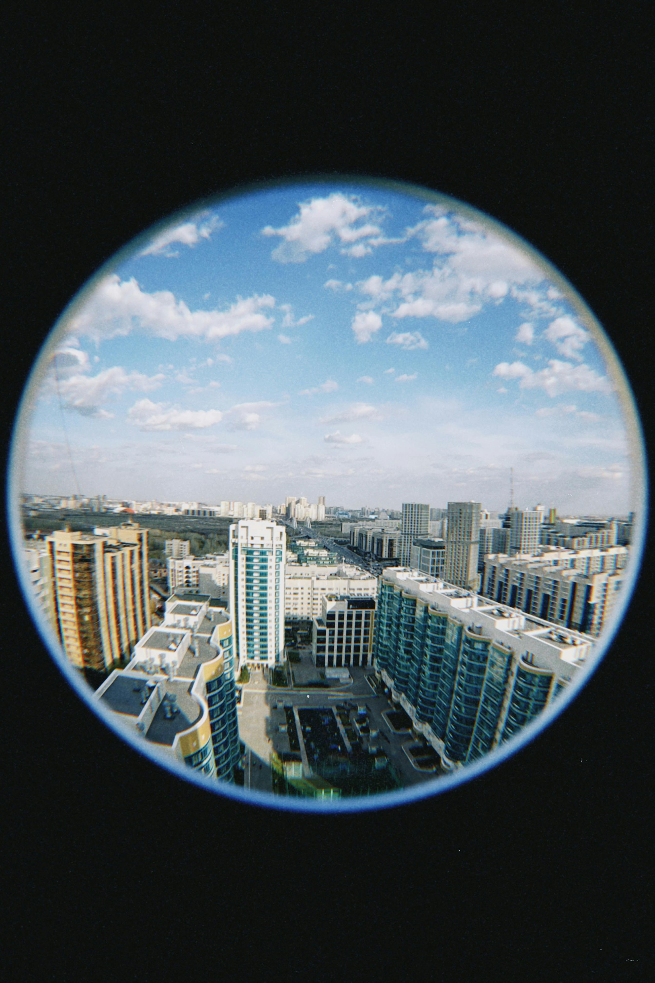 Panoramic view of Astana's modern skyline through a circular lens under blue skies.