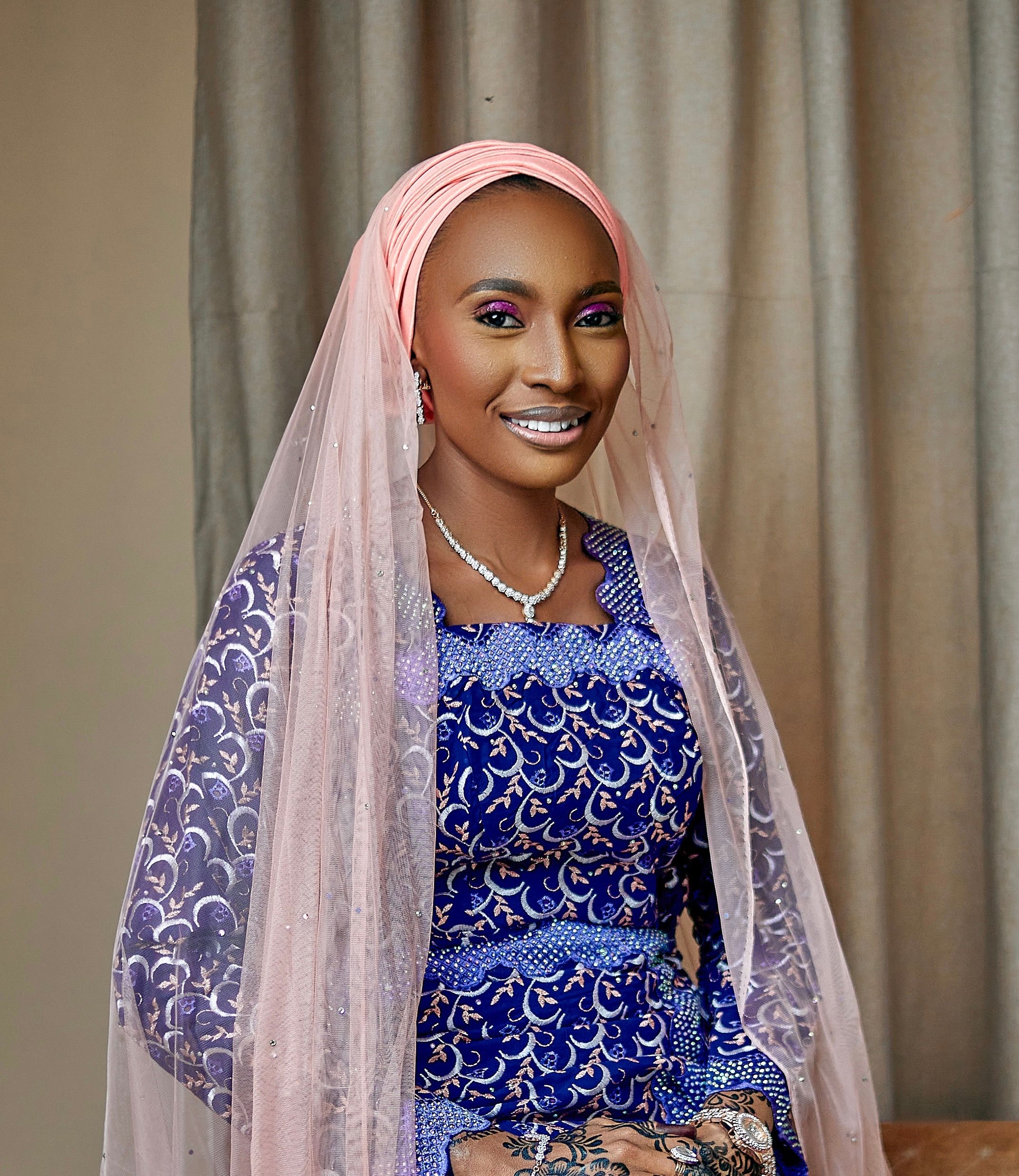 Portrait of a woman with vibrant makeup and a pink veil, wearing intricate traditional clothing.