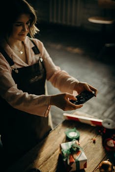 年轻女子在室内用智能手机拍摄包装好的节日礼物