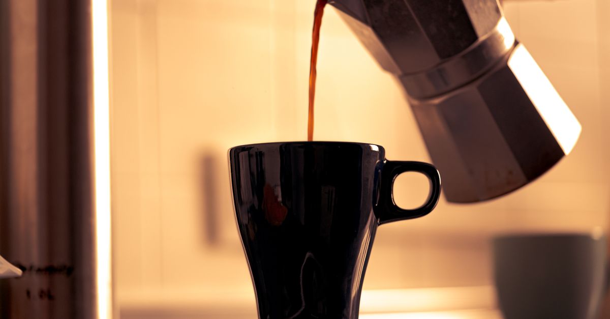 Coffee being poured slowly into a ceramic cup with steam rising