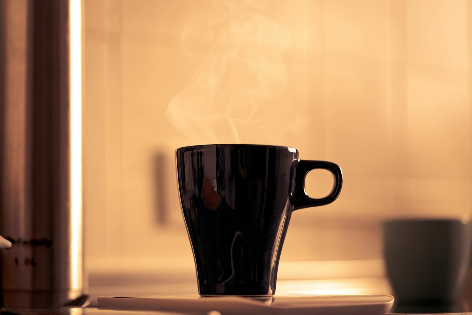 Steaming black coffee mug on saucer in warm kitchen