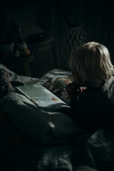 昏暗的卧室里，一个年幼的孩子正在看书，营造出舒适的氛围