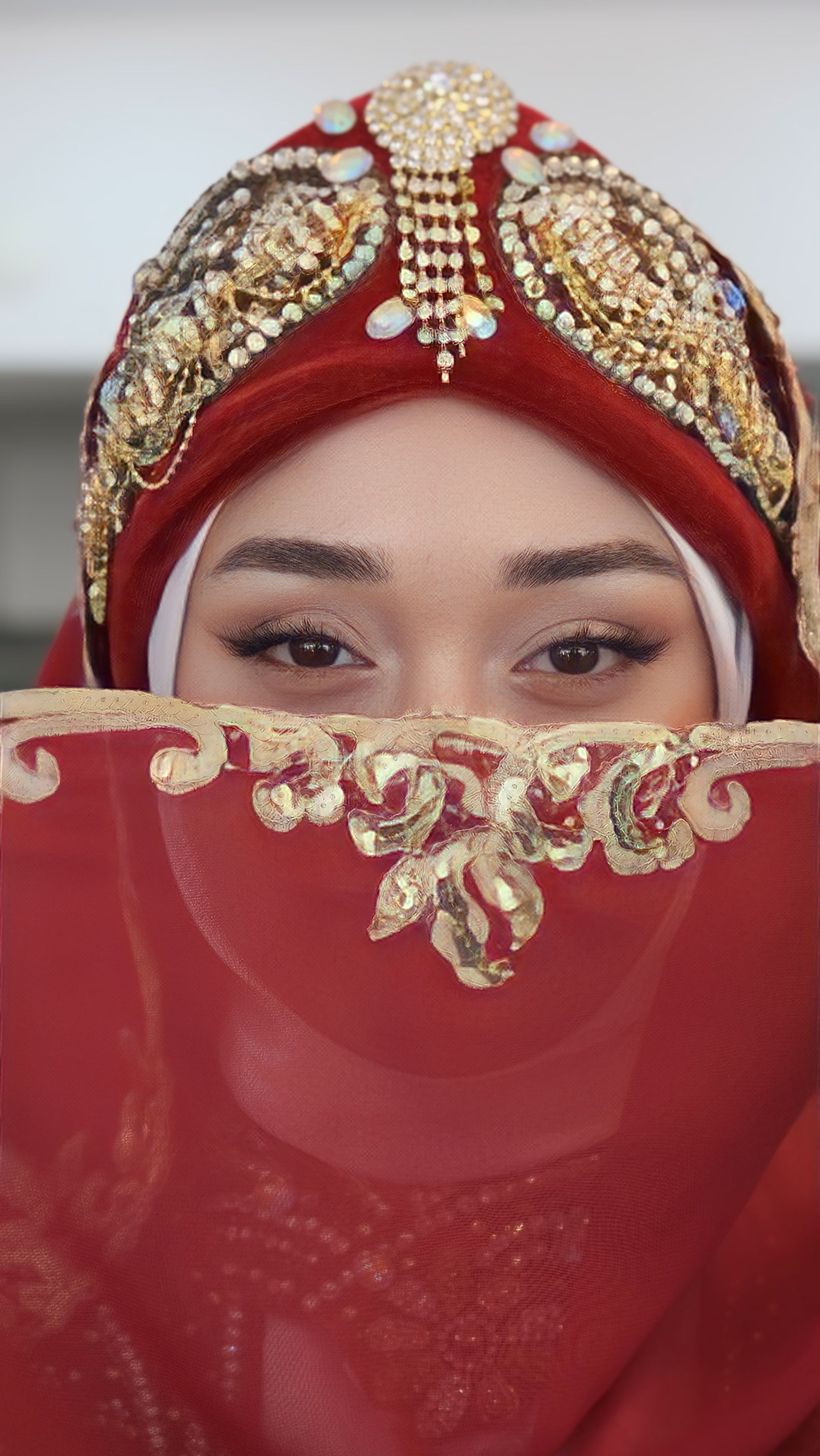 A close-up portrait of a woman in ornate red traditional attire, highlighting intricate gold embroidery.
