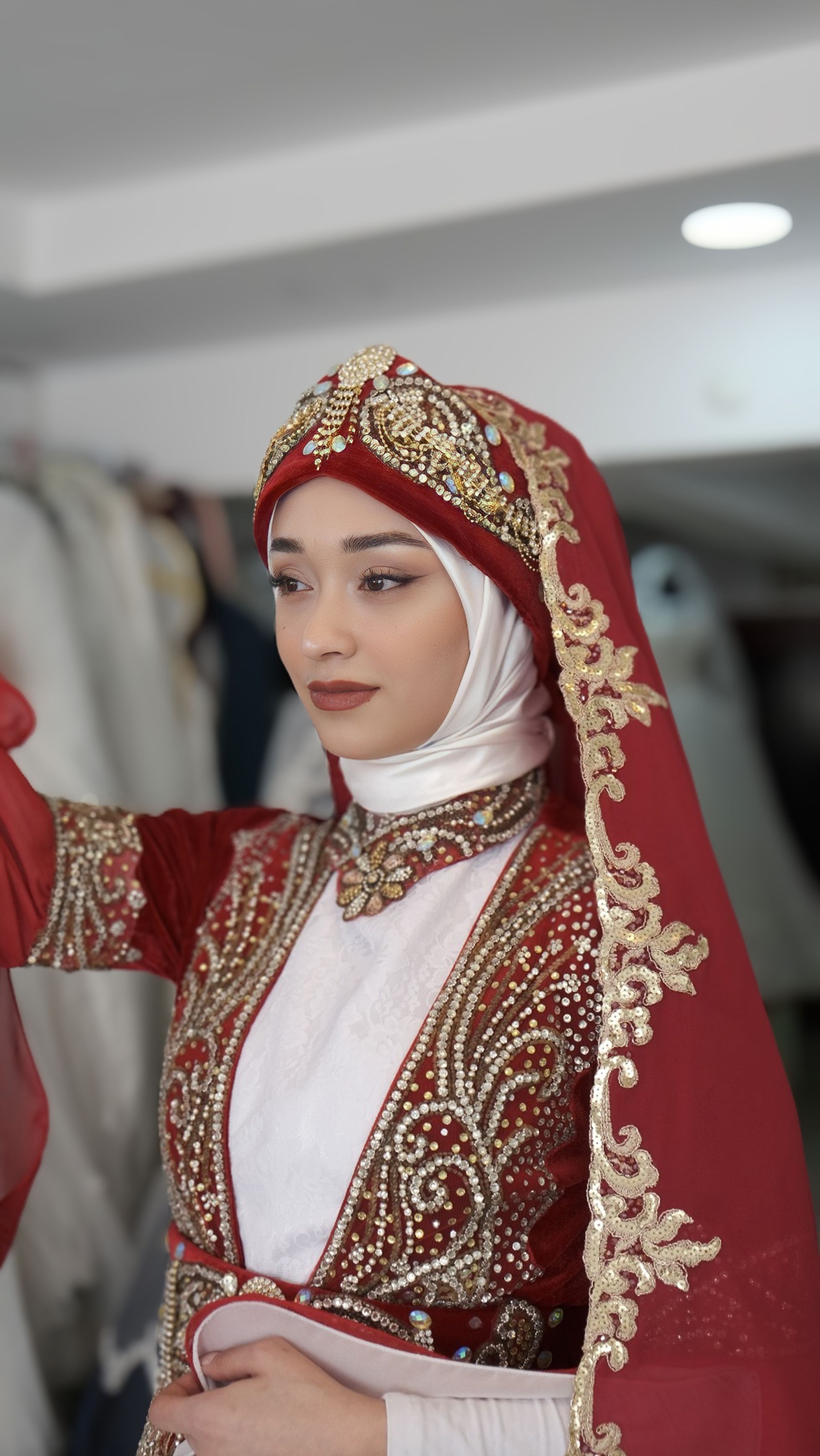 Woman in ornate red and gold traditional wedding dress, posing indoors.