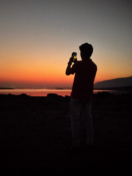 A person takes a photo of a stunning sunset over a calm river, creating a perfect evening silhouette.