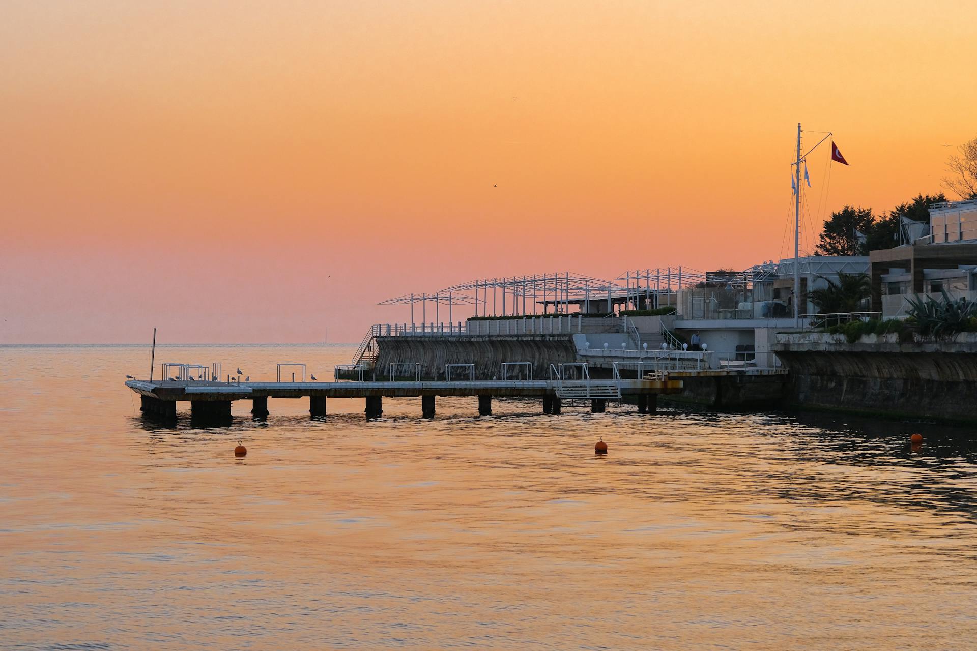 A tranquil sunset view over a seaside pier, reflecting vibrant orange hues on the water.
