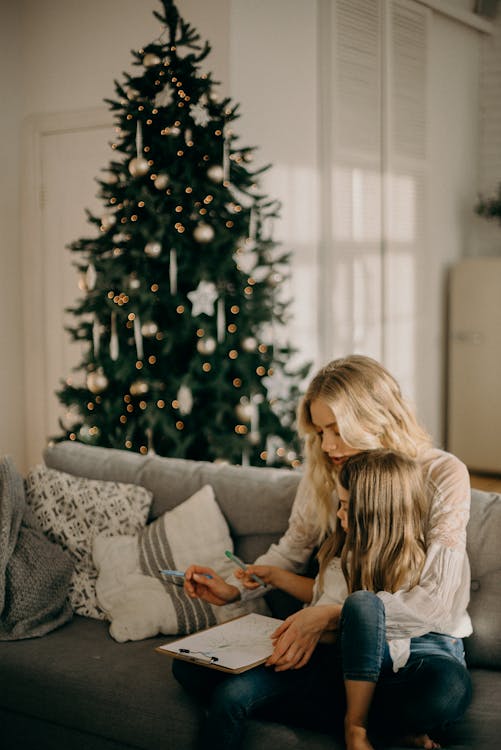 Girl Sitting on Woman's Lap While Holding Pen and Paper