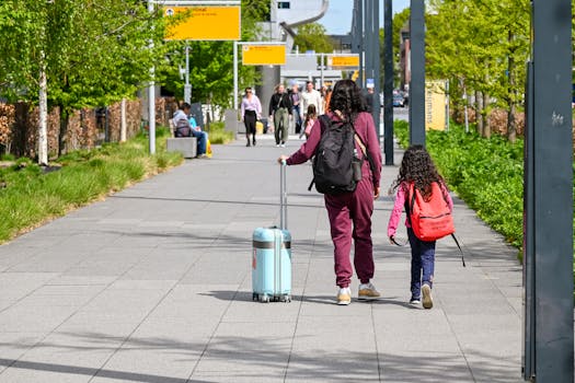 A mother and daughter walking with luggage outside Eindhoven Airport on a sunny day.