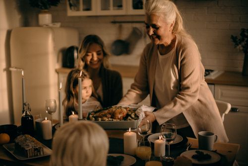 Free A grandmother serves a festive turkey dinner to family gathered around a warmly lit table. Stock Photo